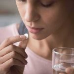 Woman holding a white pill and a glass of water