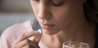 Woman holding a white pill and a glass of water