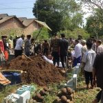 Mourners gather around a fresh grave during a burial ceremony