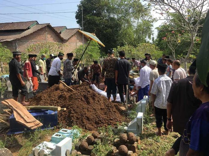 Mourners gather around a fresh grave during a burial ceremony