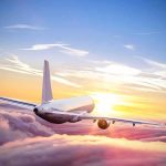 Airplane flying above clouds at sunrise