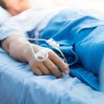 Patient hand with IV line resting on hospital bed