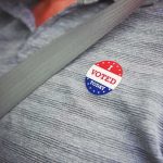 I voted sticker on a gray shirt under a seat belt