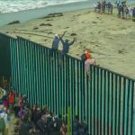 Weaponized Demography Shocks Europe People climbing a tall beachside border fence