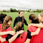 Coach talks to youth team in a huddle on a field