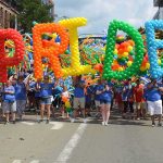 parade participants carry giant rainbow balloon letters spelling a word