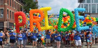 parade participants carry giant rainbow balloon letters spelling a word