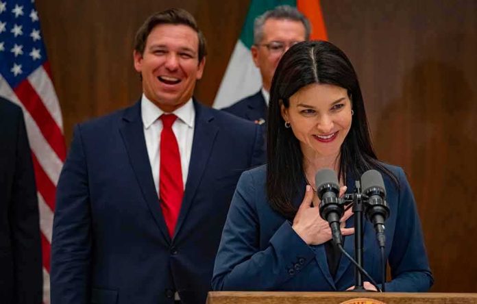 shutterstock_1355382875 Ron DeSantis smiling behind a woman speaking at a podium