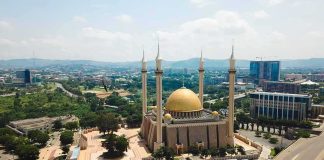 Golden-domed mosque with four minarets in a modern cityscape