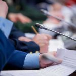 Conference microphone on table with hands holding documents