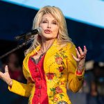 Dolly Parton performing on stage in a yellow floral jacket