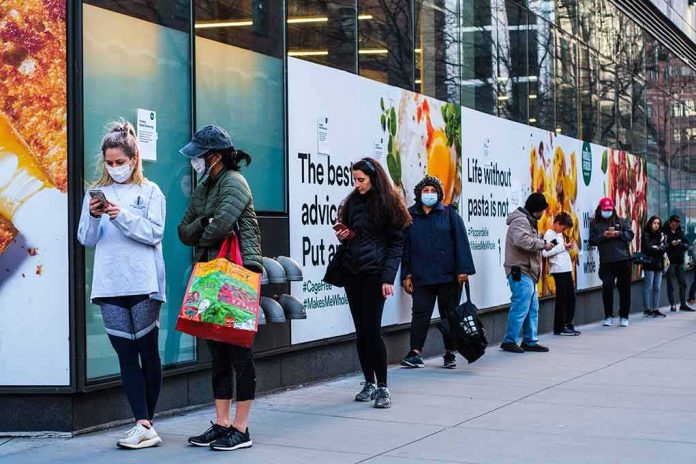 shutterstock_1690663636 People wearing masks line up outside a store on a city sidewalk