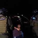 Counterterror Raids Snag Suspected Bombers Police officers detain a handcuffed person at night