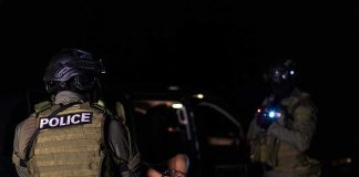 Police officers detain a handcuffed person at night