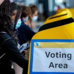voter wearing a mask using a yellow ballot box