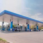 Stealth Gas Hikes Hit 26 States Gas station canopy with multiple fuel pumps and parked cars