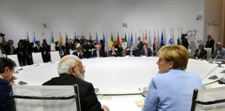 Angela Merkel and Narendra Modi seated at a large round table during an international summit