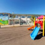 Wealthy Suburb Freezes Sprays After Kids Get Sick Playground with colorful slide in front of a school building