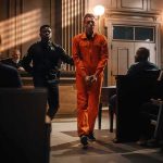 Inmate in orange jumpsuit escorted by officer in courtroom