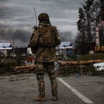 Russia’s Deal Comes With One Impossible Price Soldier in camouflage stands at roadblock with smoke in the distance