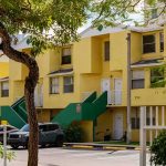 Yellow apartment building with green staircases and parked cars