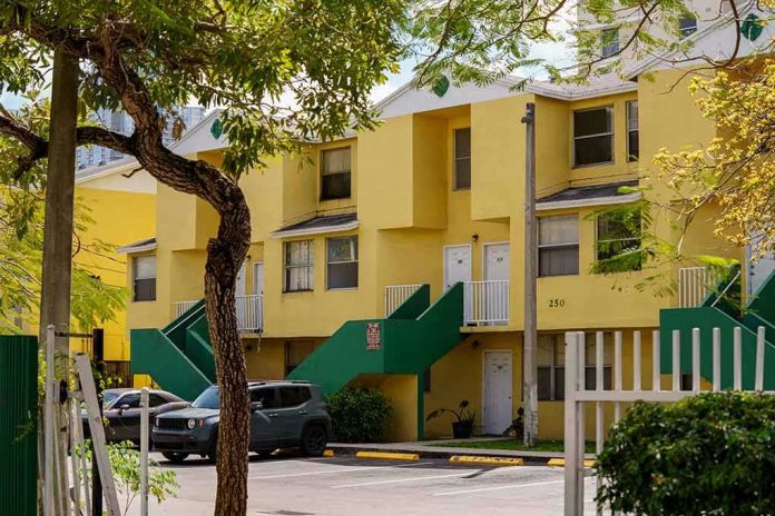 shutterstock_2132728047 Yellow apartment building with green staircases and parked cars
