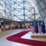 Europe’s Migration Crackdown — What It Does and Why Critics Are Alarmed Row of national flags in a modern glass atrium with red carpet and EU and US flags upfront