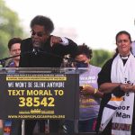 Cornel West speaking at a rally podium with supporters behind him