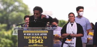 Cornel West speaking at a rally podium with supporters behind him