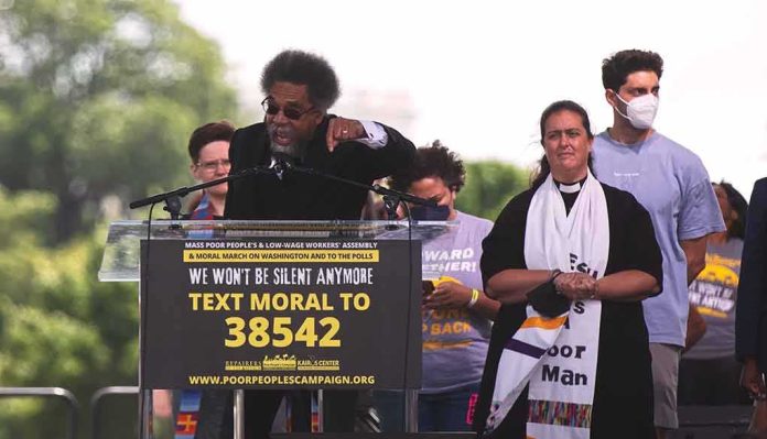 Cornel West speaking at a rally podium with supporters behind him