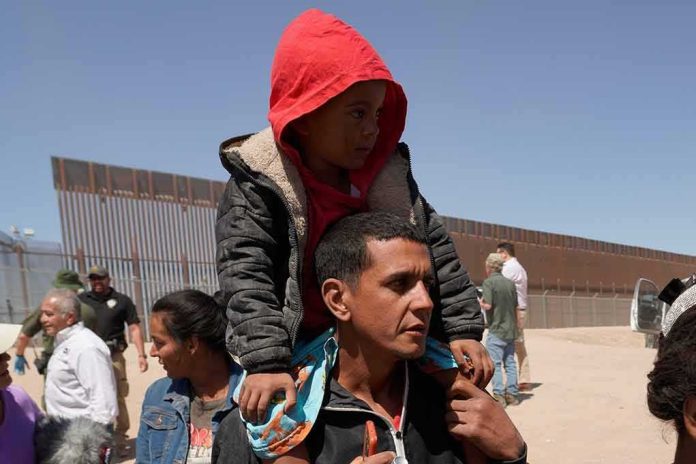 shutterstock_2301352311 Man carrying a child in a red hoodie on his shoulders near a border fence