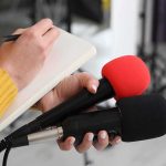 SpaceX Keeps Its Launch Machine Moving Journalist holding two microphones while writing in a notebook