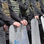 Riot police line holding metal shields