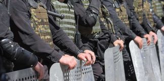 Riot police line holding metal shields