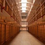 Prison cellblock corridor with barred cells and upper walkways