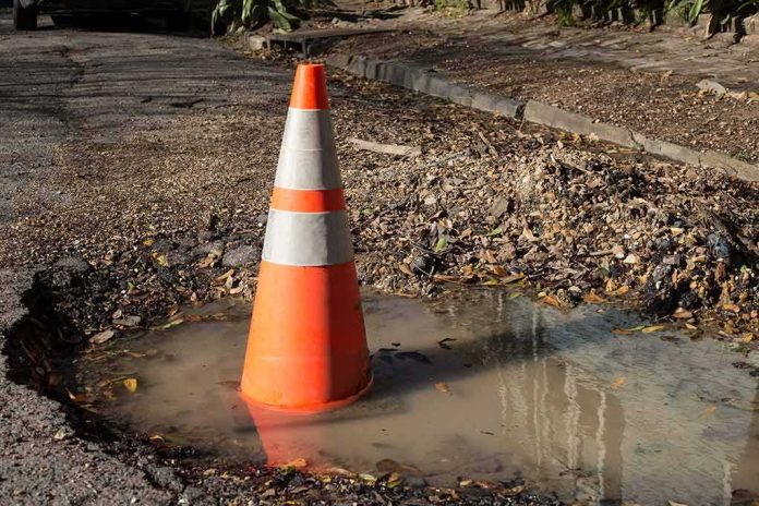 Traffic cone in a water-filled pothole on a damaged road
