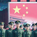 China-Russia Pact: U.S. In Crosshairs? Group of uniformed soldiers standing before a large red flag