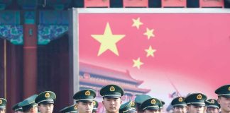 Group of uniformed soldiers standing before a large red flag