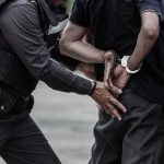 Police officer handcuffing a person against a vehicle