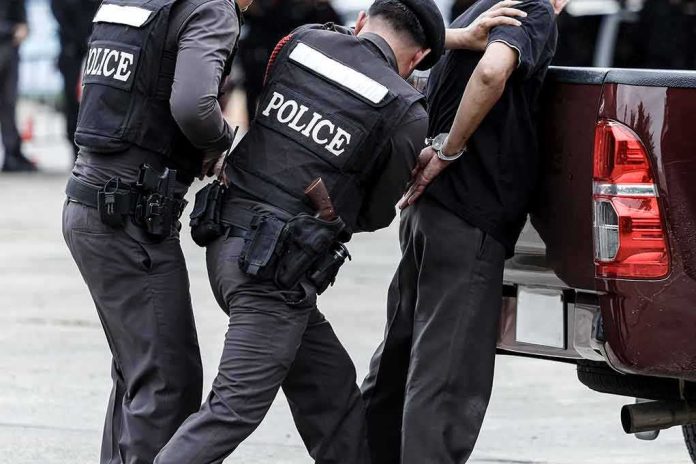 Police officers detain a handcuffed man beside a pickup truck