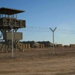 Guard tower beside barbed-wire fence in desert camp