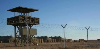 Guard tower beside barbed-wire fence in desert camp