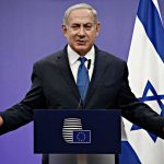 Netanyahu Delivers a Chilling Warning to London man in suit speaking at a podium with Israeli flag