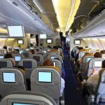 Co-Pilot Rampage Midair – Cockpit Breached Interior view of an airplane with passengers seated and using in-flight entertainment screens