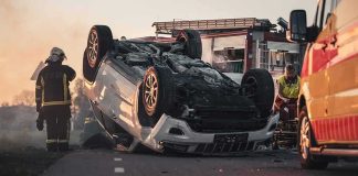 Overturned car on road with firefighters and ambulance