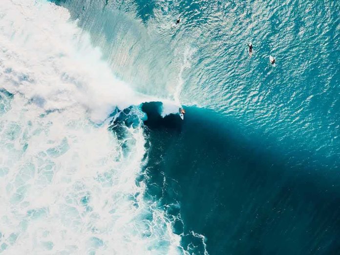 Surfer riding a large turquoise wave from above