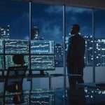 Trader in a dark office with multiple stock monitors and city skyline at night