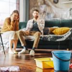 Buckets catching water leak in living room with couple on couch