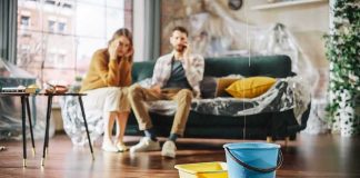 Buckets catching water leak in living room with couple on couch