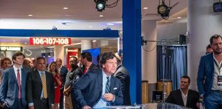 Tucker Carlson at a news desk with Carter Beauford among the onlookers